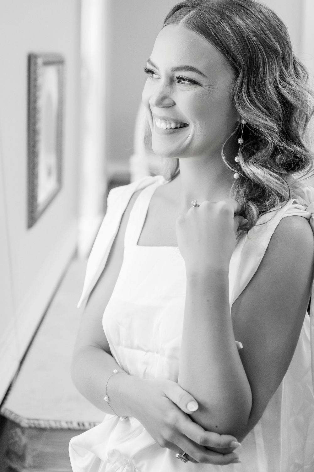 Black and white portrait of a joyful bride in a white dress with elegant wavy hair and jewelry.