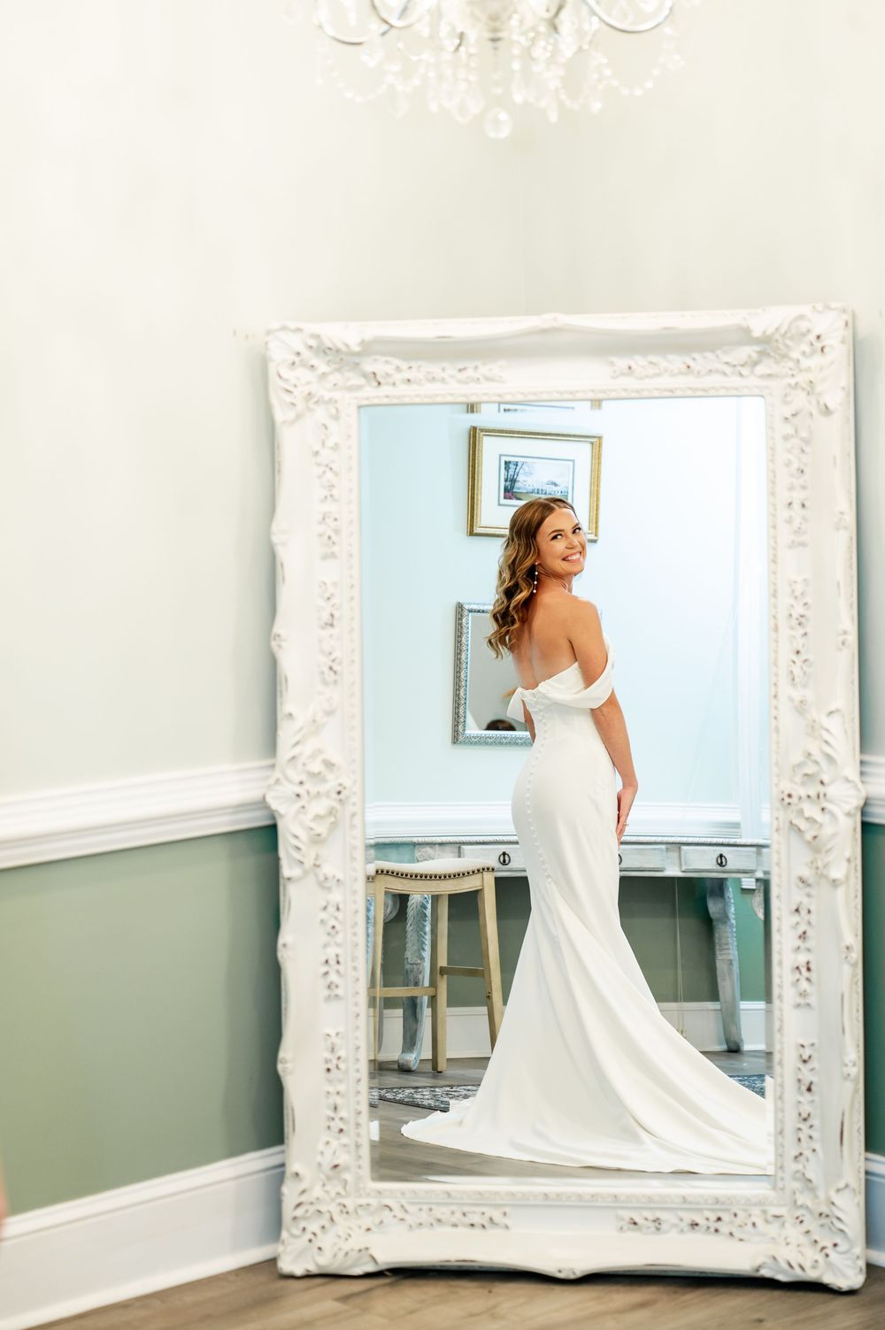 Wedding dress reflections in an ornate white frame mirror against mint green walls.