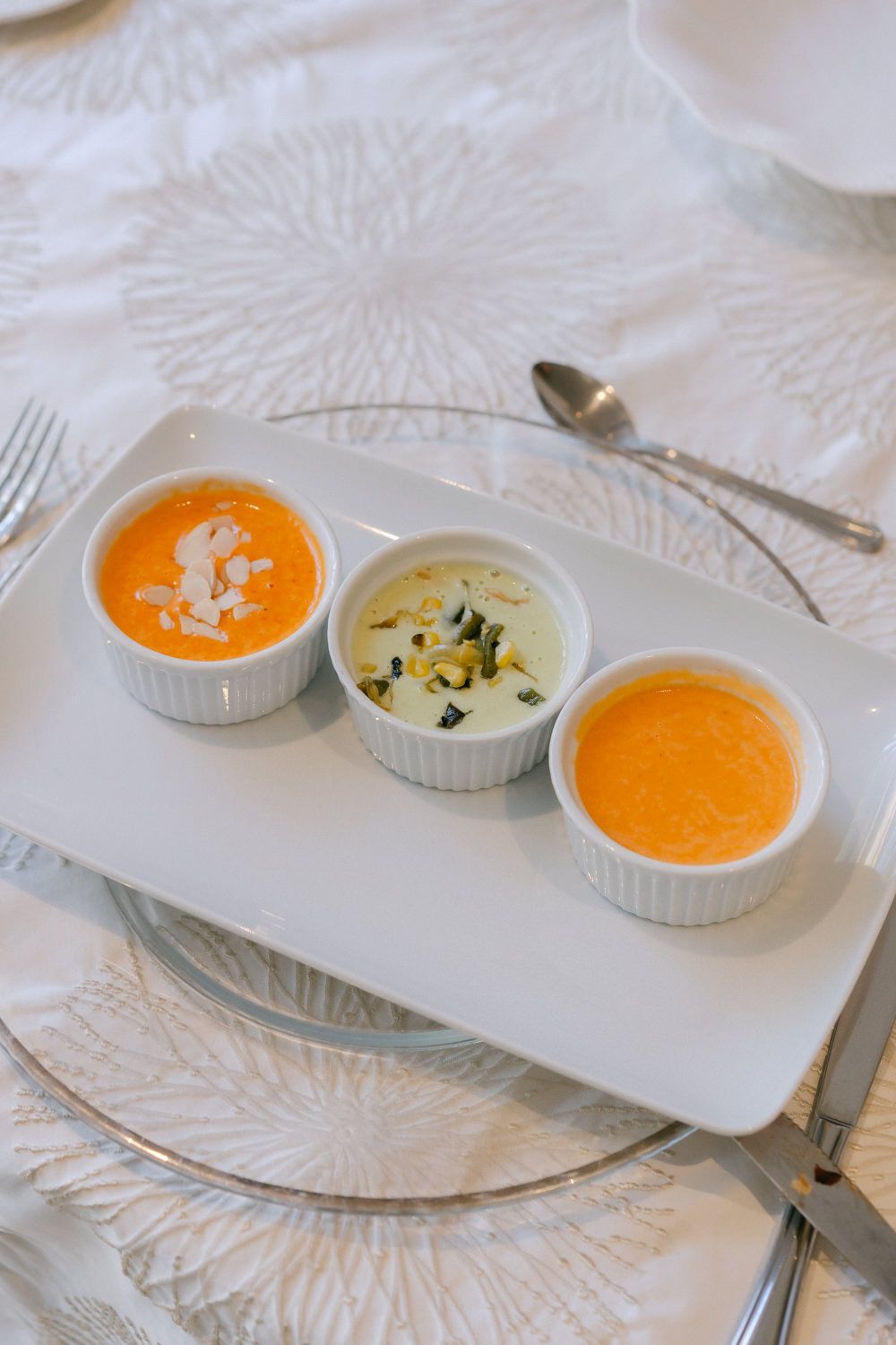 Three small white ramekins filled with orange and cream-colored soups arranged on a white serving platter.