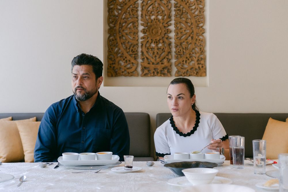 Two diners seated at an elegant restaurant table with white tablecloth looking off to the side.