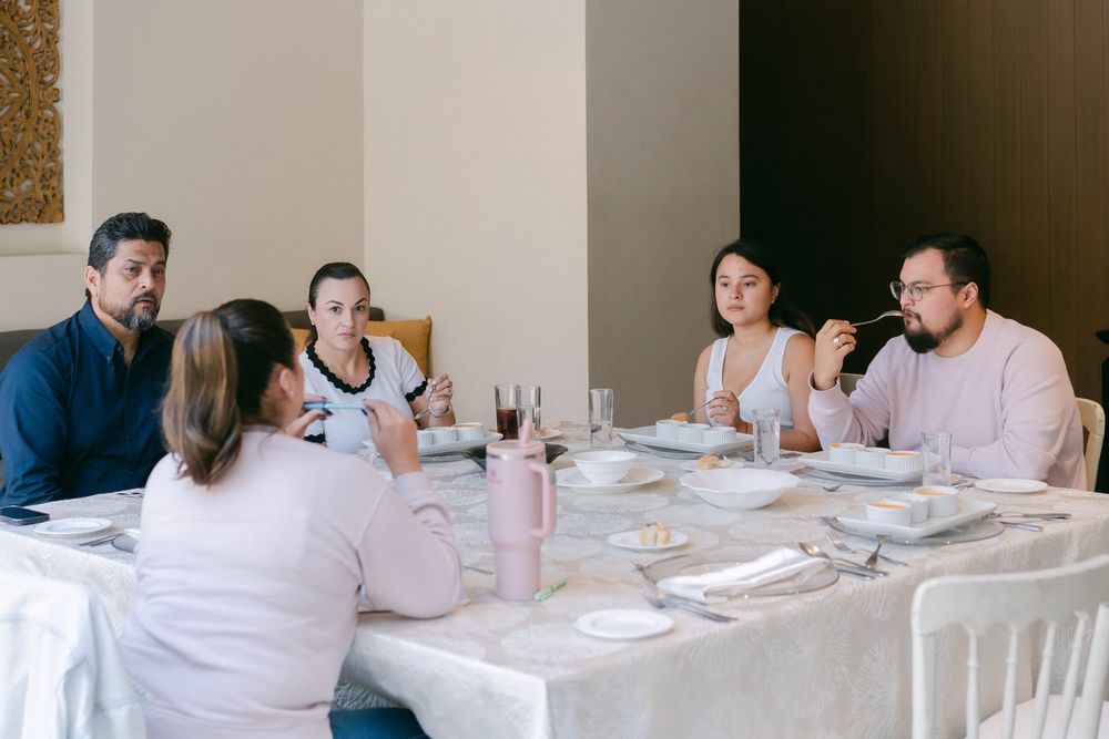Diners seated at a long white table in an elegant restaurant setting enjoying a meal together.