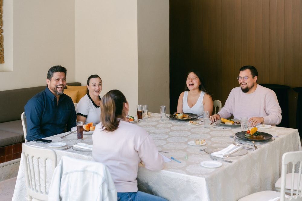 People seated at a long white-clothed dining table enjoying a formal meal in an elegant indoor setting.
