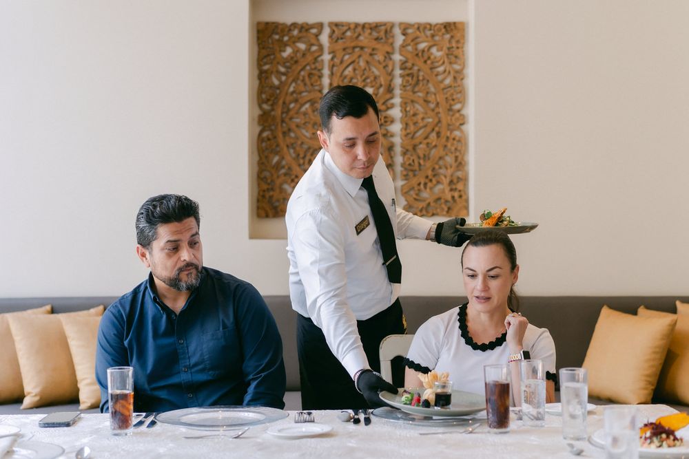 Business colleagues sit at a long table during a casual lunch meeting in a modern office setting.