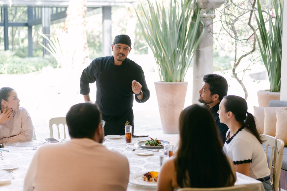 Diners seated at a bright, modern restaurant with white tablecloths and large windows.