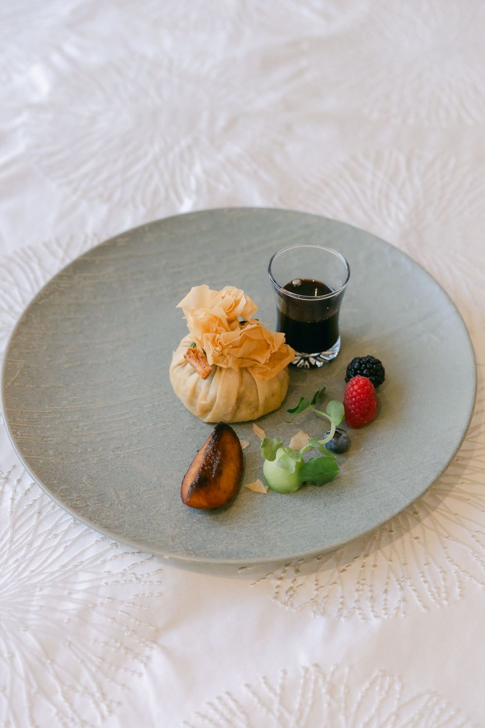 Fine dining dessert plate with pastry, fresh berries and dark sauce served on a gray ceramic dish.