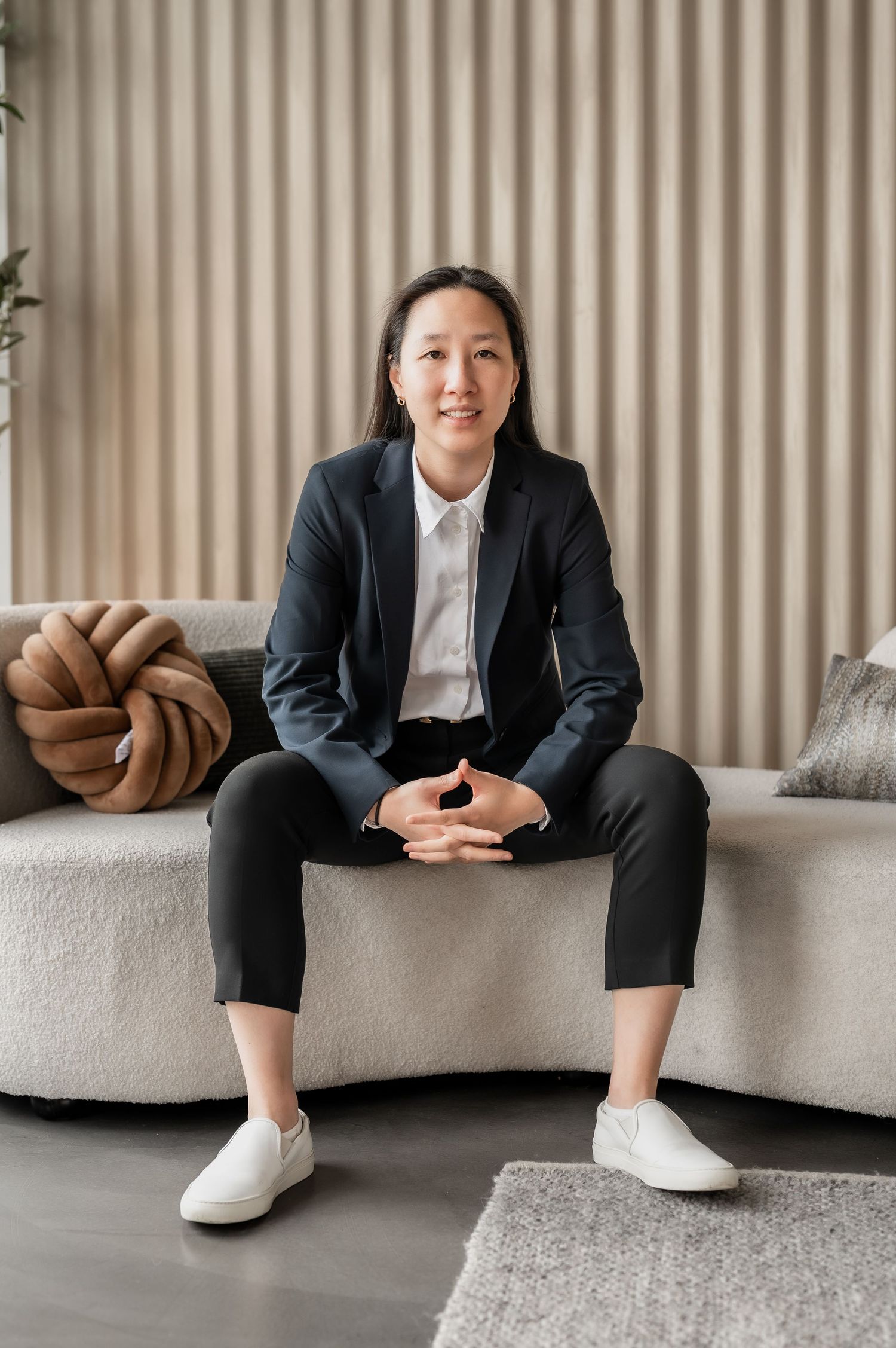Professional sitting on gray couch wearing black suit and white sneakers shown from different angles in modern setting.