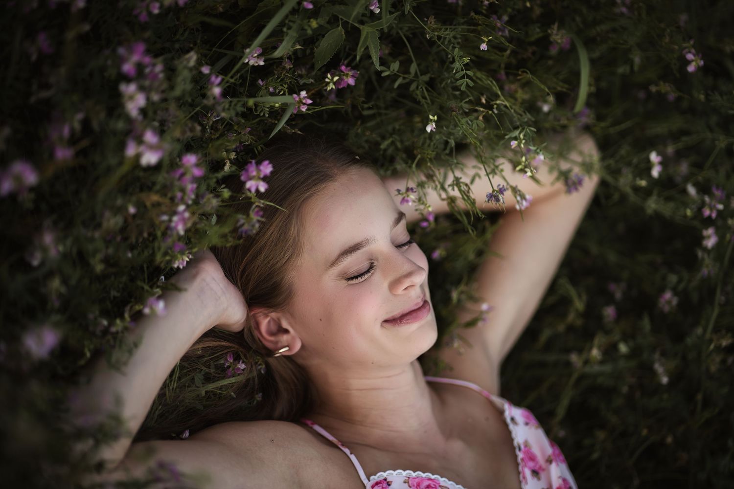 Young woman with eyes closed lying peacefully among wildflowers  smiling serenely in natural light at senior session in Arlington Heights