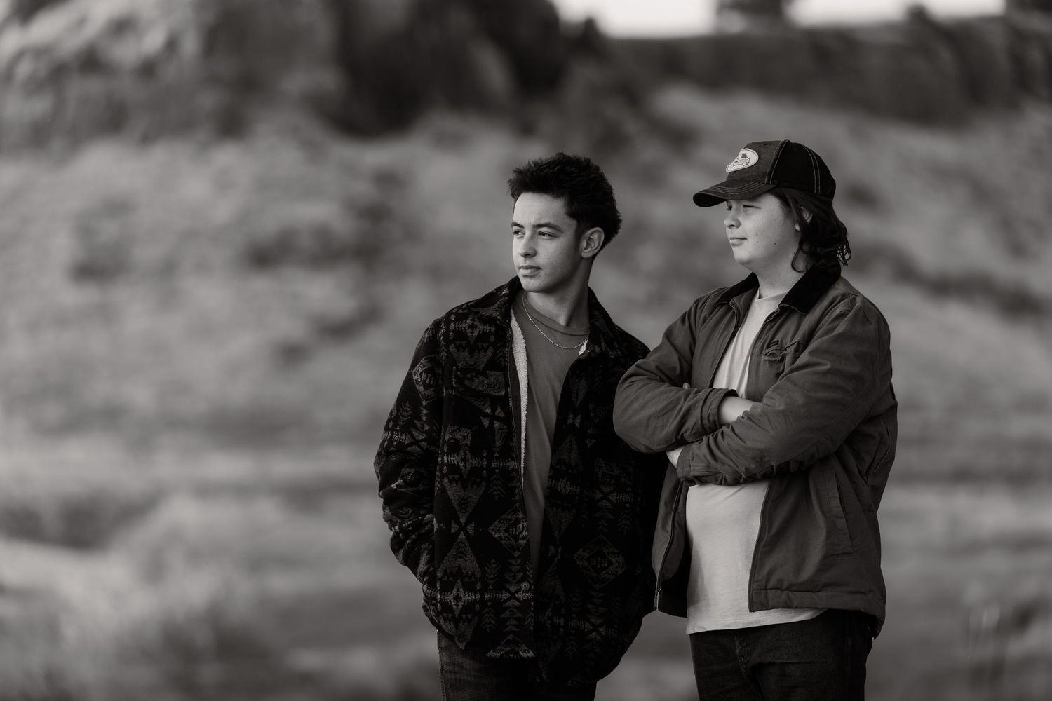 Black and white photo of a couple posing with a large tractor or construction vehicle in a rural setting.