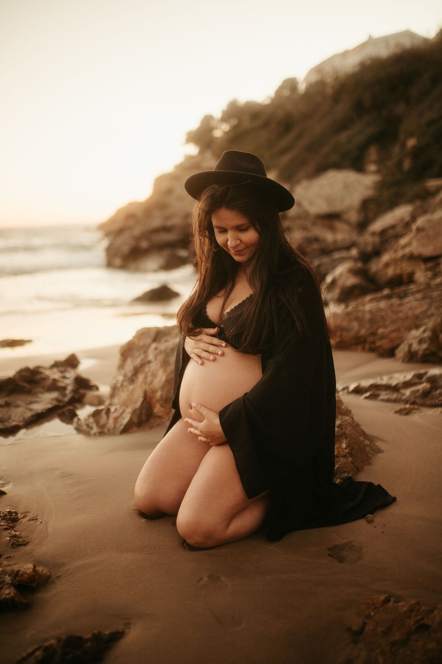 Mujer embarazada de rodillas en la orilla del mar acariciando su barriga en Tarragona