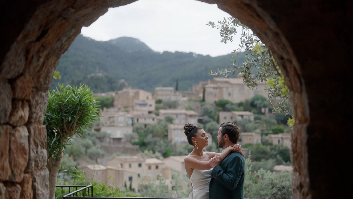 Bride and groom dancing under a stone arch with views of a picturesque mountain village. Shot by Timeless weddings Mallorca videographer