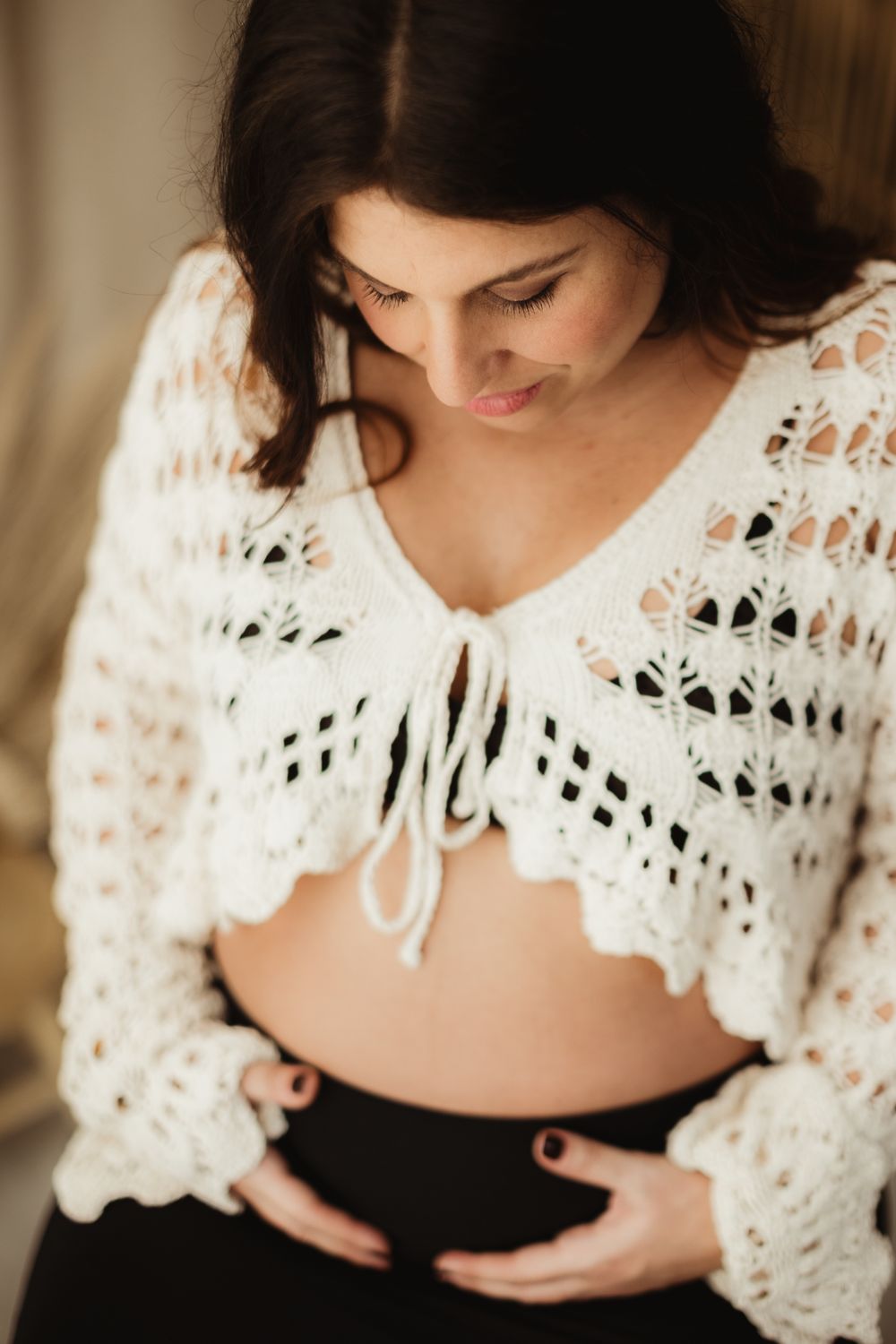 A woman in a white crocheted shawl sits in soft lighting while breastfeeding her baby.