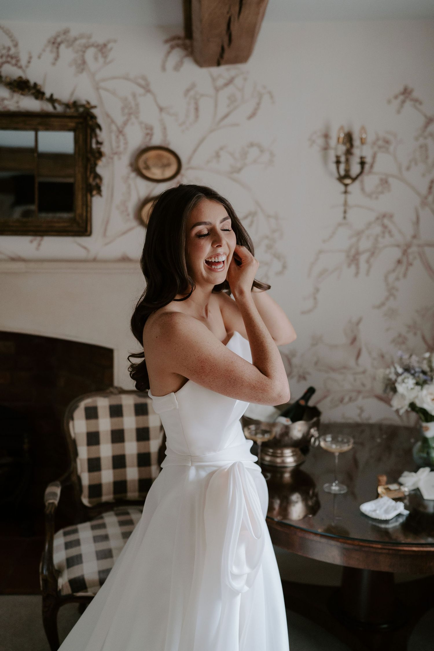 bride fastening her earrings and laughing at dewsall court in herefordshire