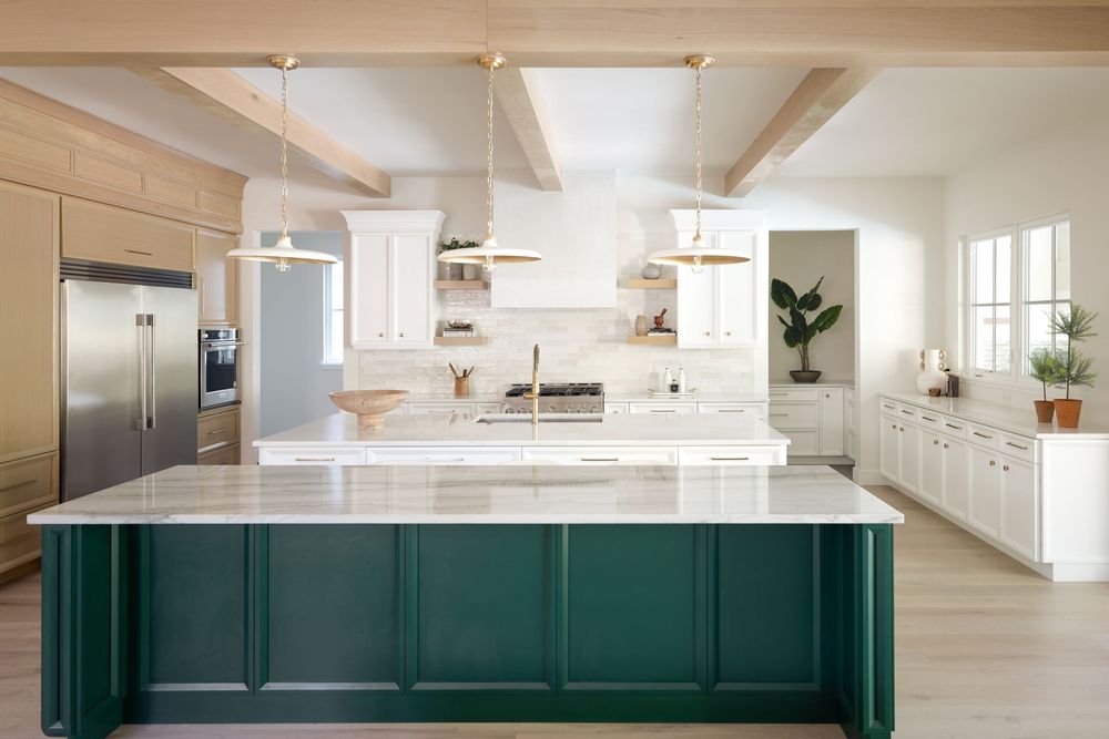 Bright kitchen with dark green island, white cabinets, marble countertop, and gold pendant lights.