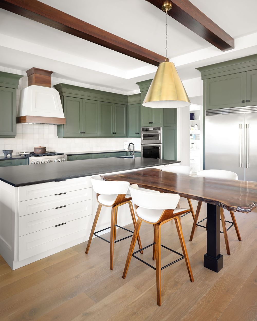 Transitional kitchen with sage green upper cabinets, black countertops, wood island, and brass pendant light.