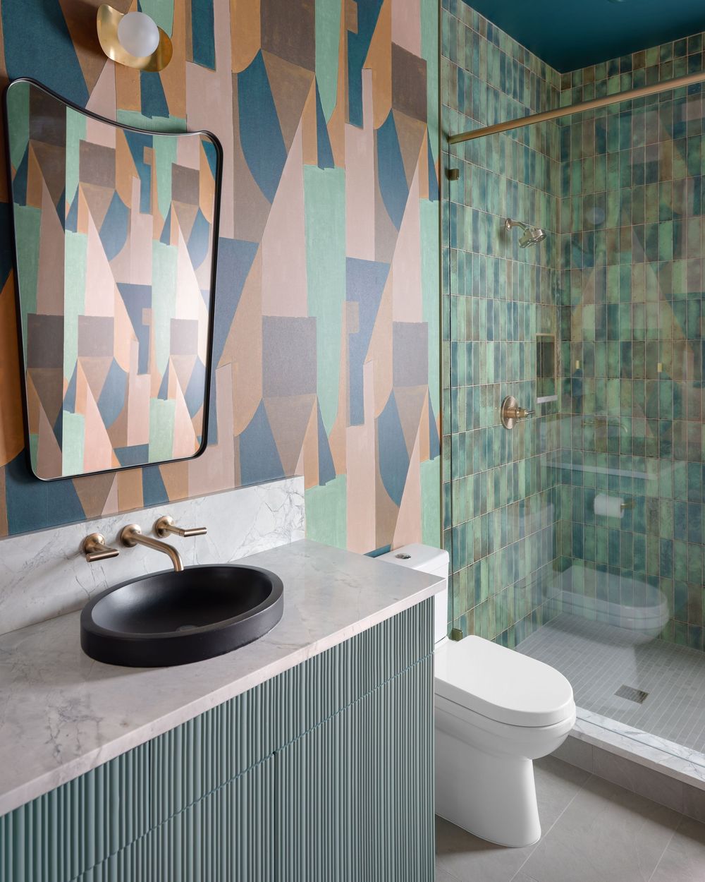 Bold bathroom with geometric wallpaper, teal zellige shower tiles, black vessel sink, and brass fixtures.
