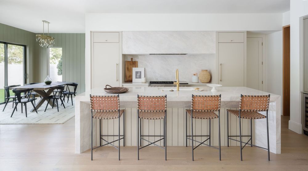 Bright open kitchen with cream cabinetry, marble backsplash, leather woven barstools, and adjacent dining area.