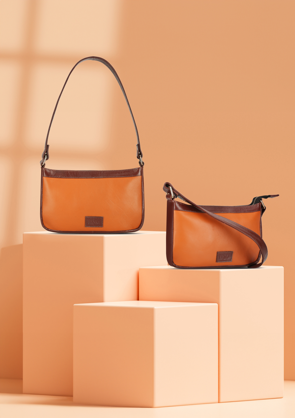 Two orange leather crossbody handbags with brown trim displayed on peach geometric blocks against a warm beige background.