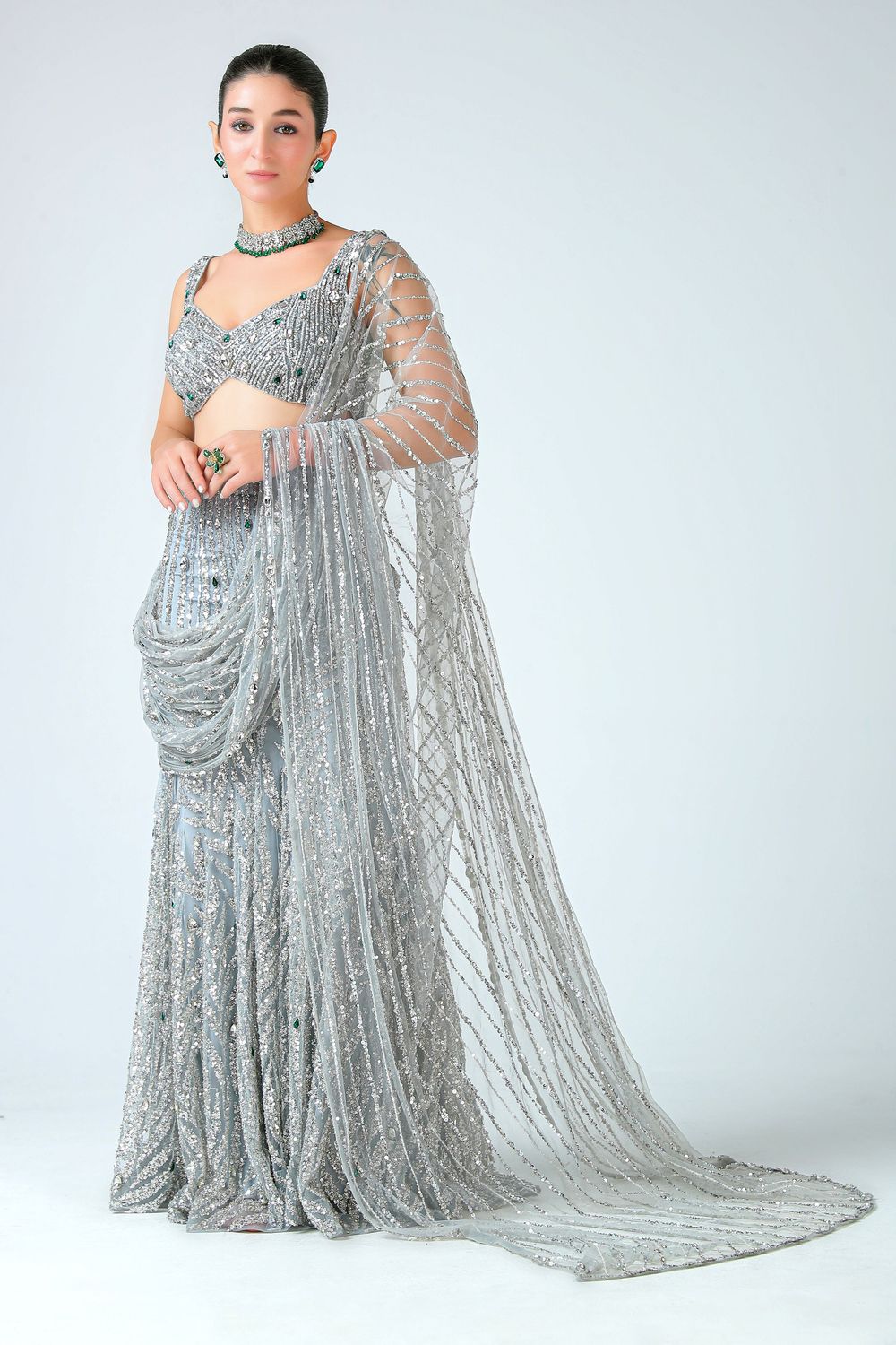 Woman wearing a silver embellished lehenga saree with intricate beadwork, sheer dupatta, and matching choker necklace.