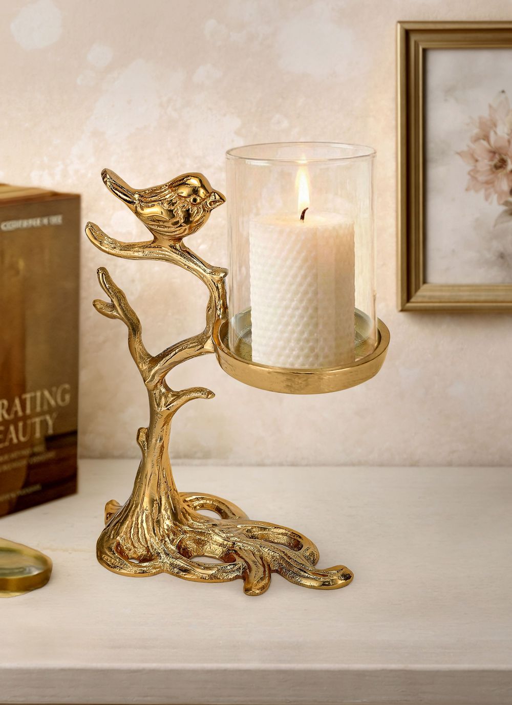 Gold bird on branch candle holder with glass hurricane and lit pillar candle, decorative metal tree sculpture.