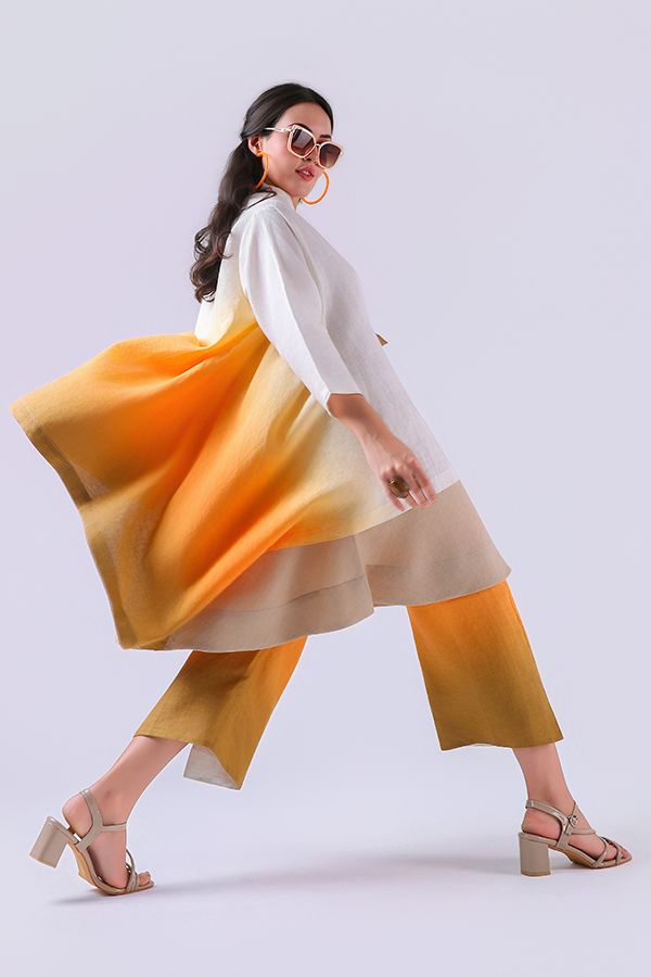 Woman posing in orange ombre midi dress with wide-leg pants, sunglasses, and beige block heels on white background.