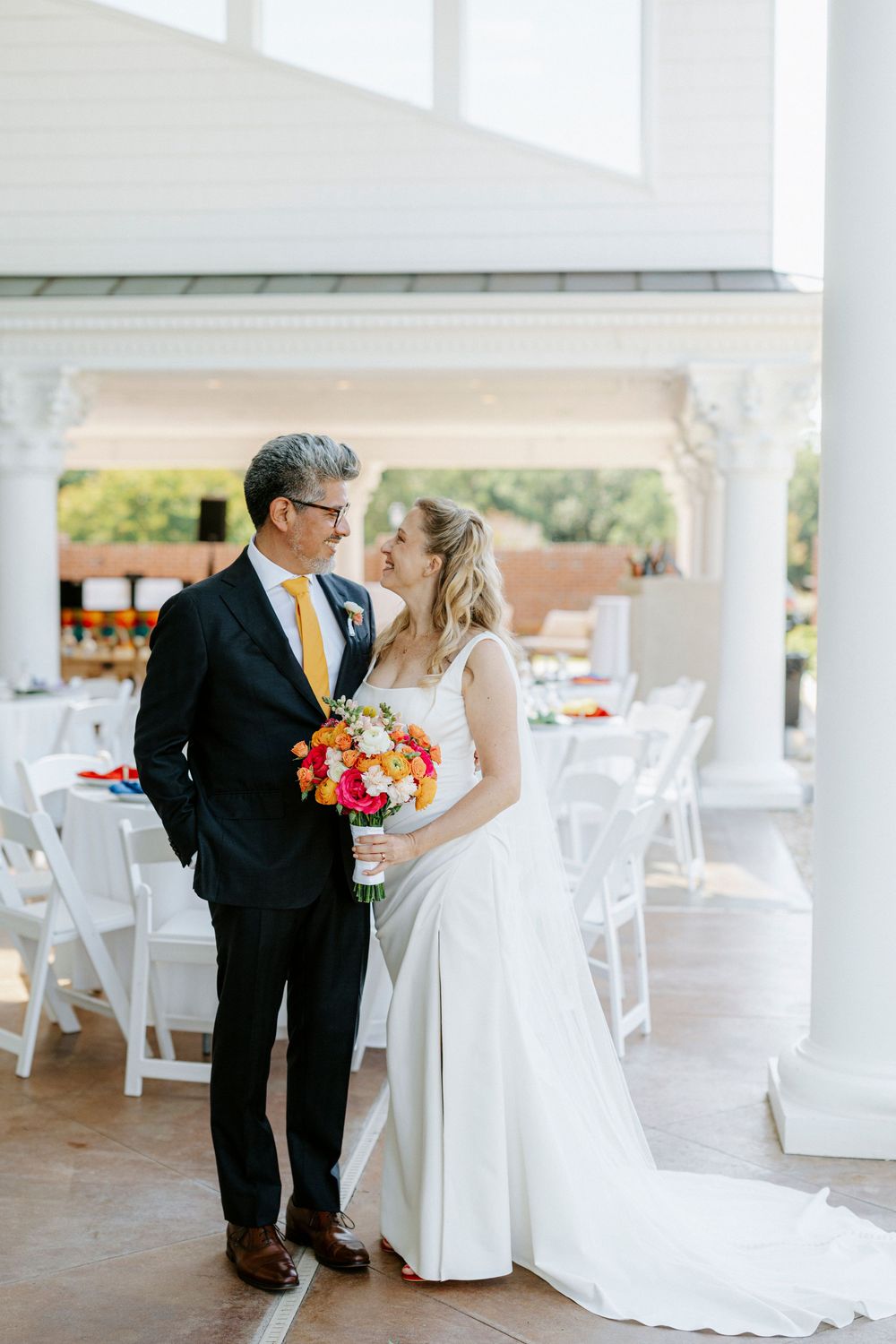 Bride and groom share a romantic moment outdoors at elegant wedding venue with white chairs and colorful bouquet.