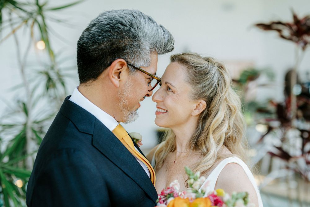 A bride and groom share a tender moment, smiling at each other, with the bride holding a colorful bouquet.