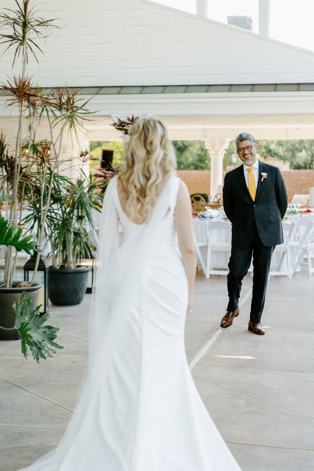 Bride in white gown with cape train faces groom in dark suit with yellow tie during wedding first look.