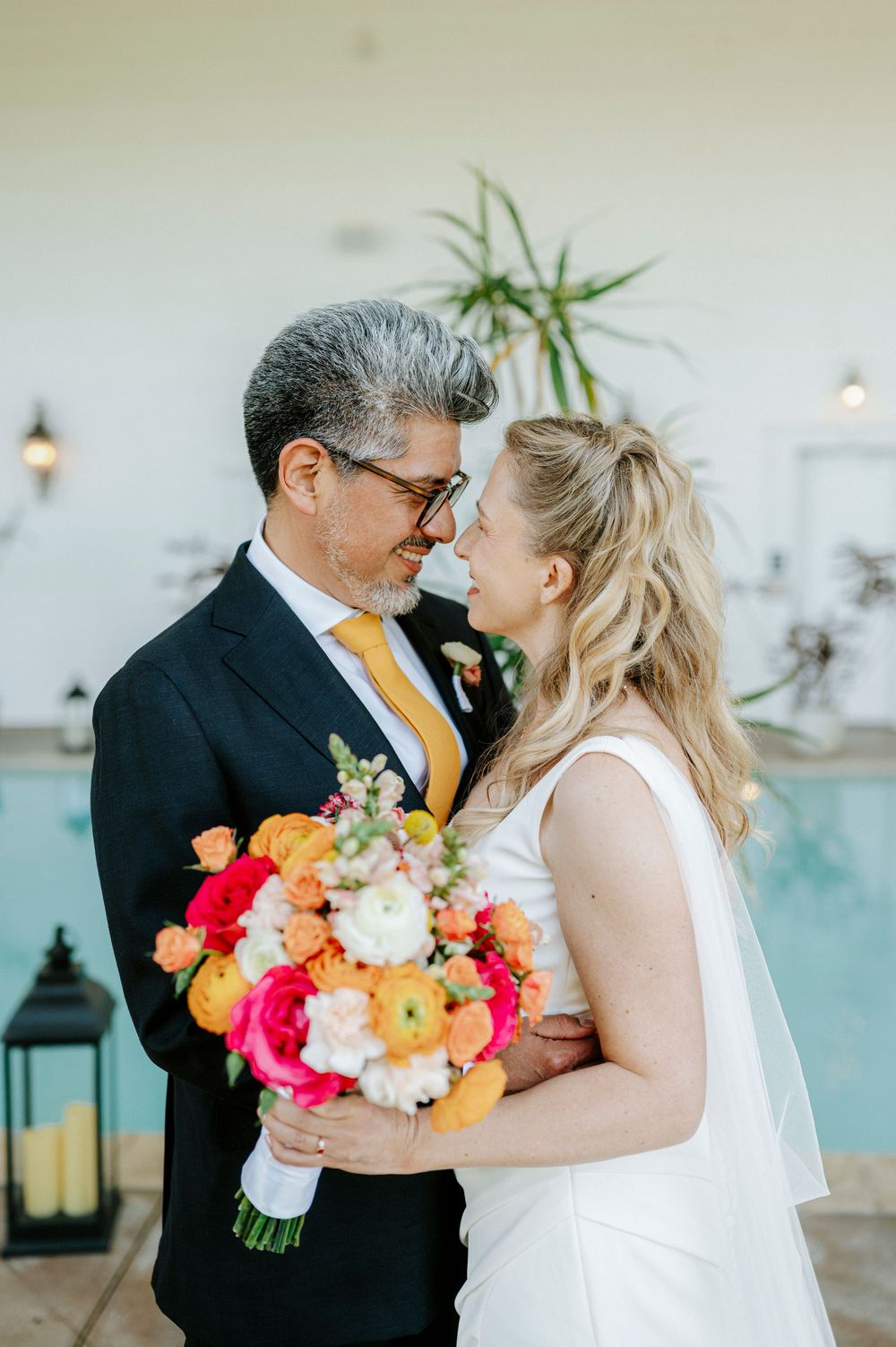 Bride and groom share romantic moment holding vibrant orange and pink bouquet during outdoor wedding portraits.