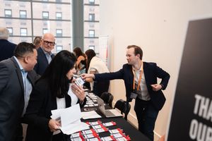 Professionals networking at a conference registration table, exchanging business cards and documents in a modern venue.