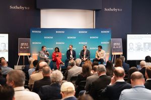 Panel discussion at Bisnow real estate conference held at Sotheby's, featuring seven speakers on stage before a packed audience.