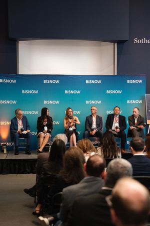 Panel of seven speakers on a Bisnow-branded stage presenting to an audience at a professional real estate conference.
