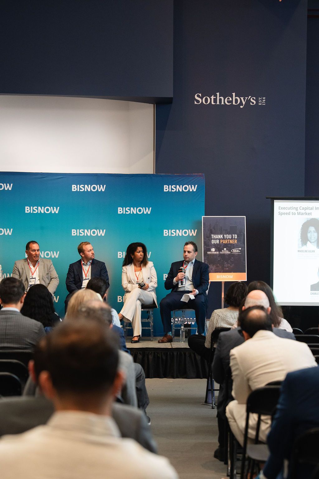 Panel discussion at a Bisnow event hosted at Sotheby's, featuring four speakers seated on stage before an audience.