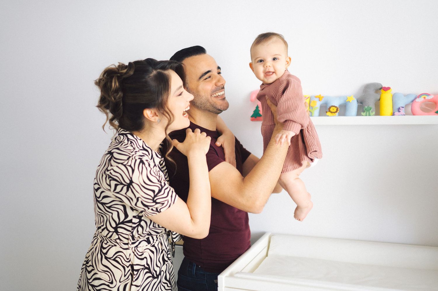 Parents lovingly tend to their newborn baby on a changing table in a bright, floral-decorated nursery room.