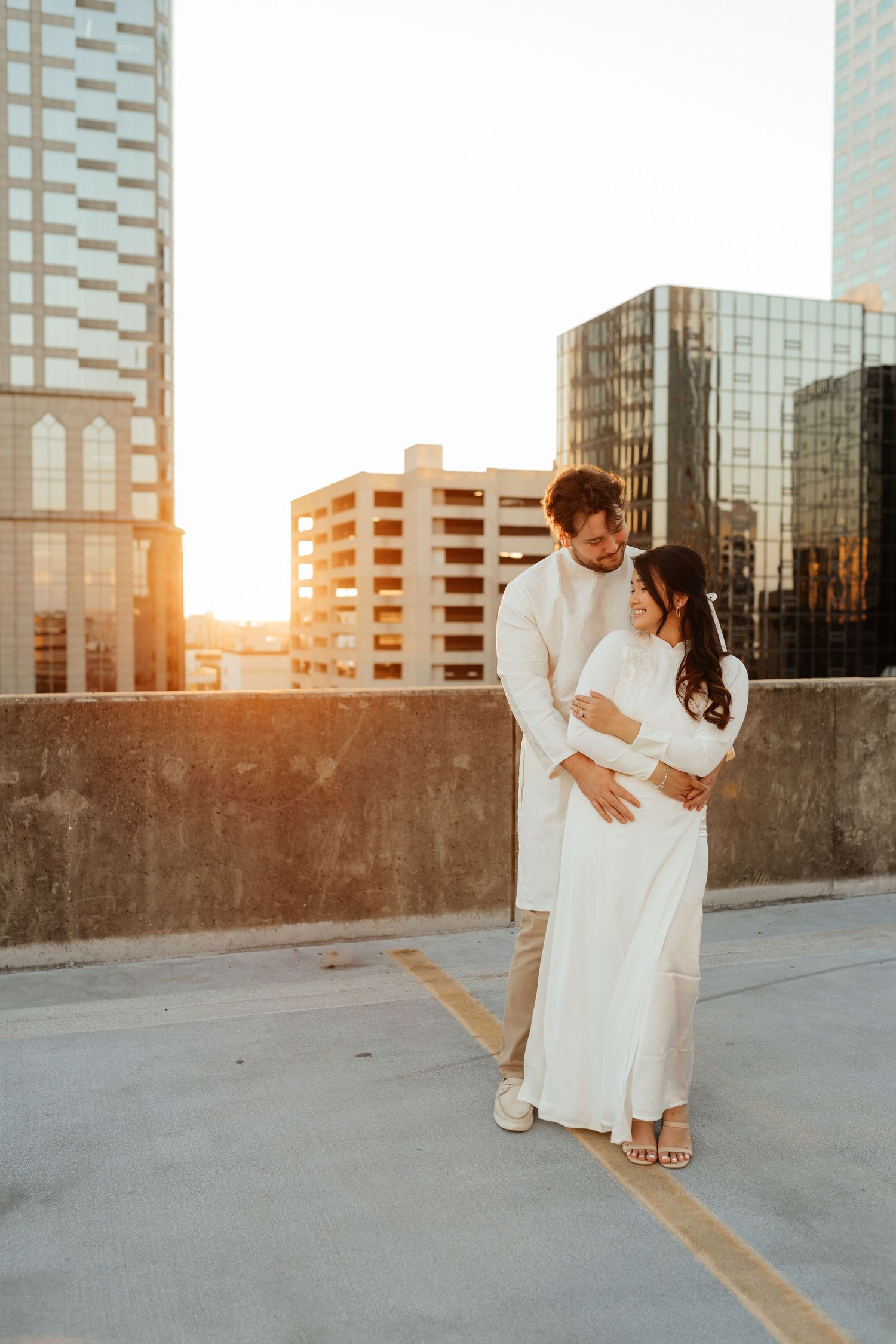 Romantic lifestyle couple photo taken on a rooftop with city buildings in the background at sunset.