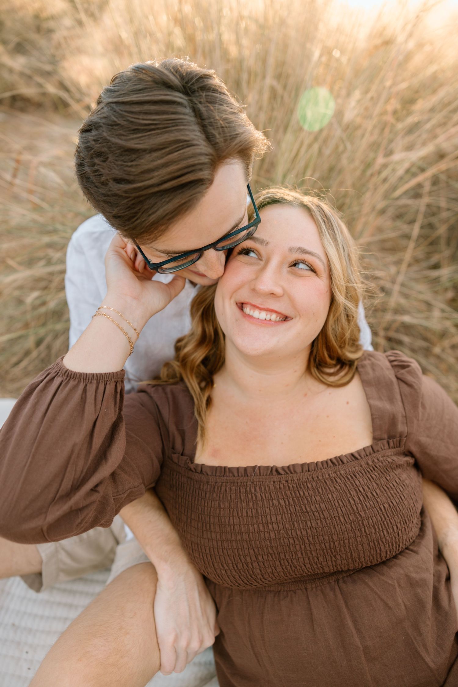 Lifestyle couple session featuring a playful embrace in tall grass during golden hour.