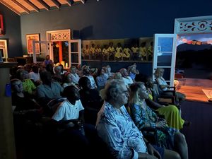 Audience seated in a small theater watching a presentation in a warmly lit venue with colorful decor.