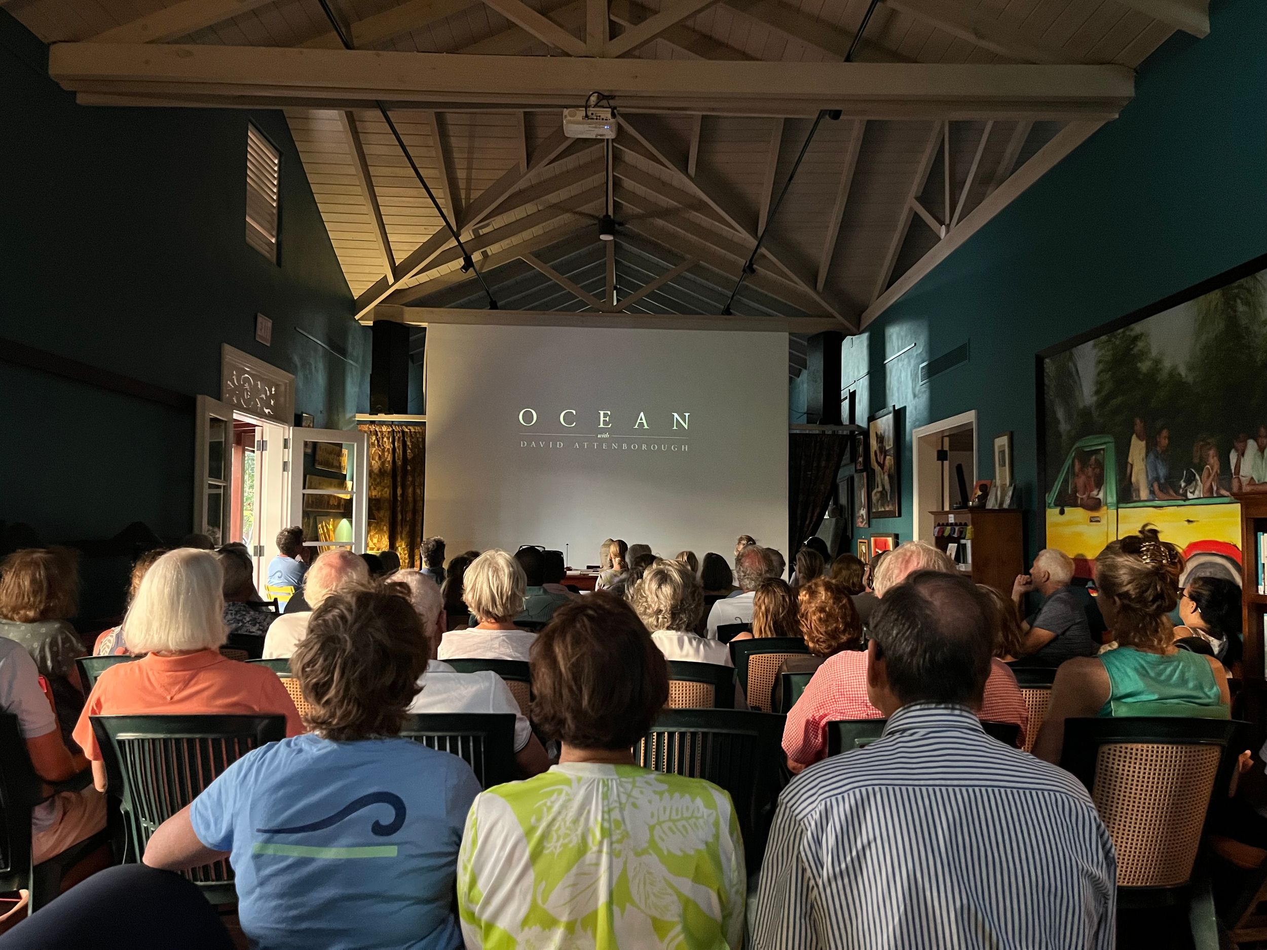 Audience watching an OCEAN film screening in a rustic gallery venue with vaulted ceilings and artwork on teal walls.