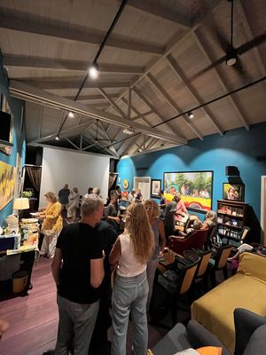 Guests mingle at a vibrant art gallery with teal walls, colorful paintings, and exposed beam ceilings during an opening event.