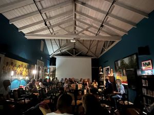 Crowded indoor venue with blue walls, vaulted ceiling, and audience seated for an evening event or presentation.