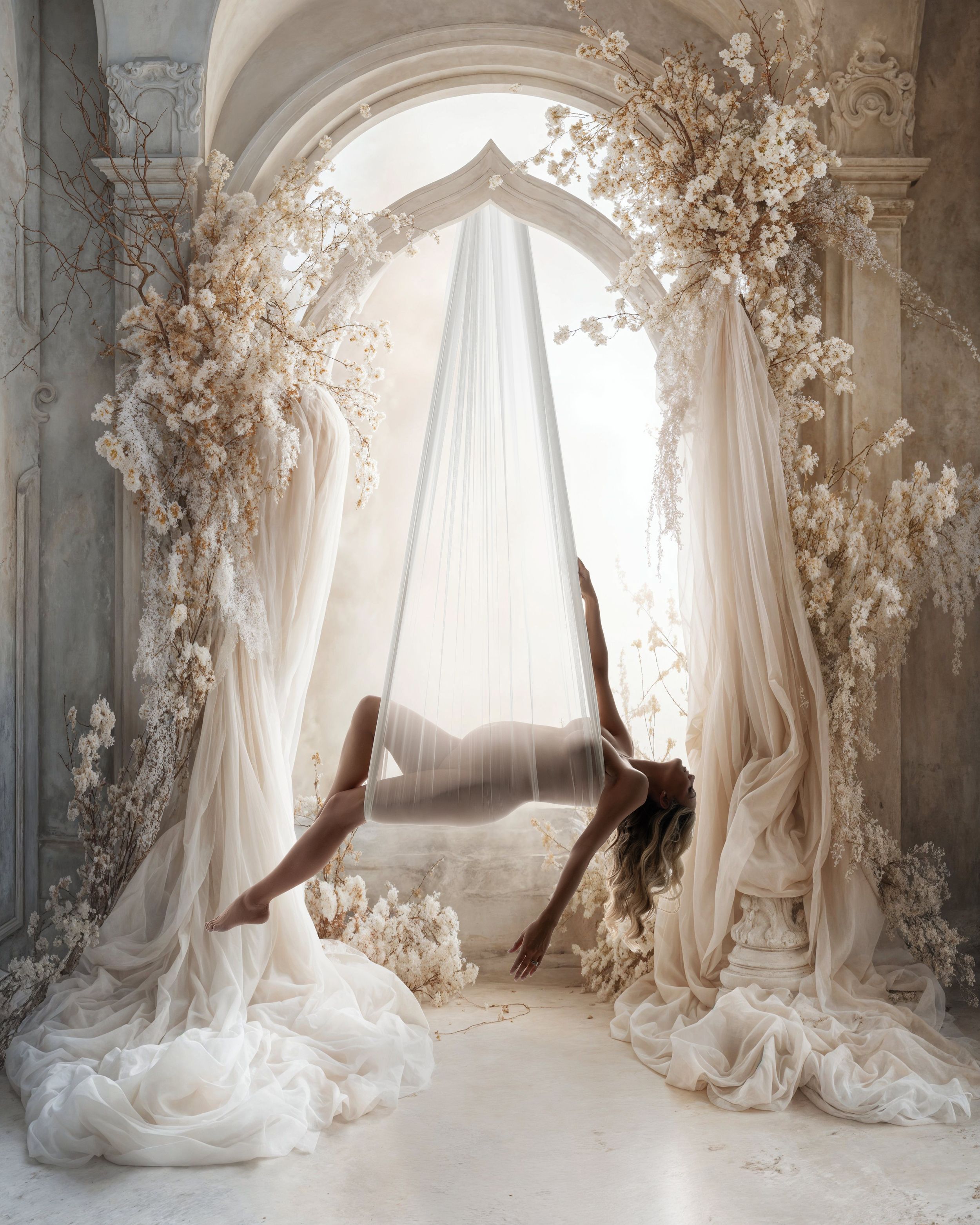 Ethereal aerial dance performance in a white archway decorated with delicate floral arrangements and flowing curtains.