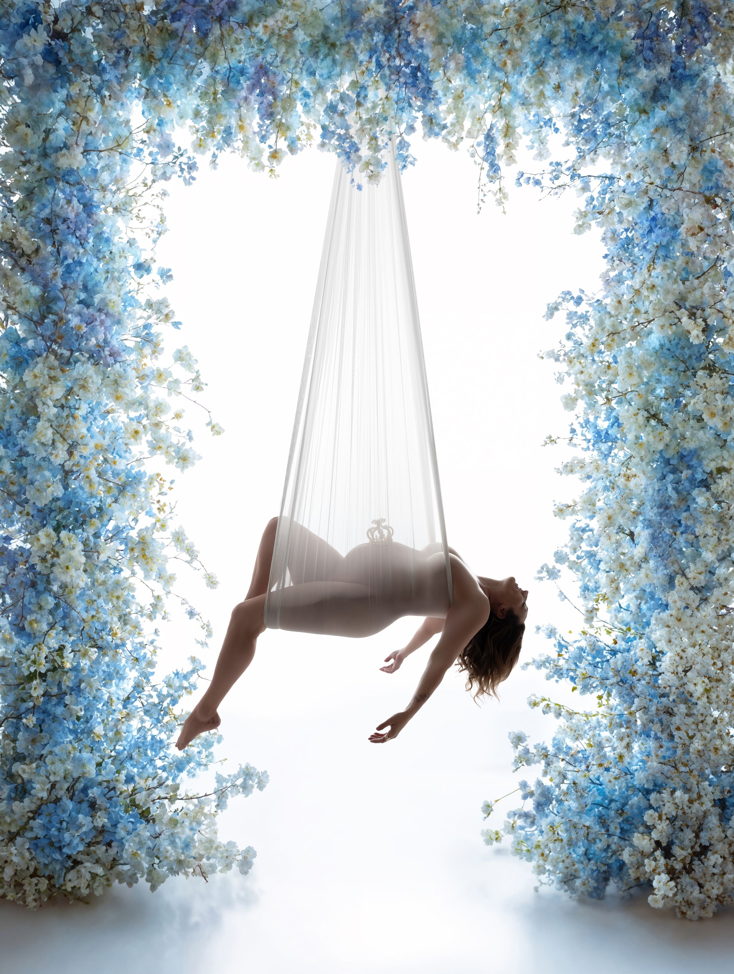 A dreamy composite of someone floating in sheer white fabric against a soft blue floral backdrop shows ethereal movement.