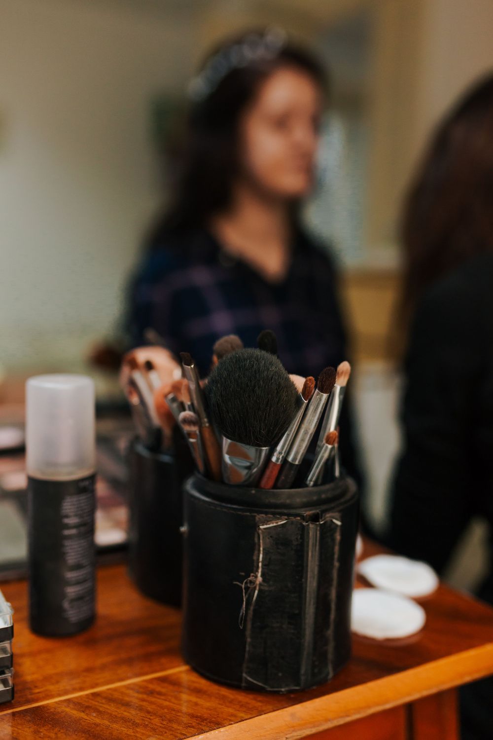 Professional makeup brushes organized in black holders on wooden vanity table during bridal preparation.