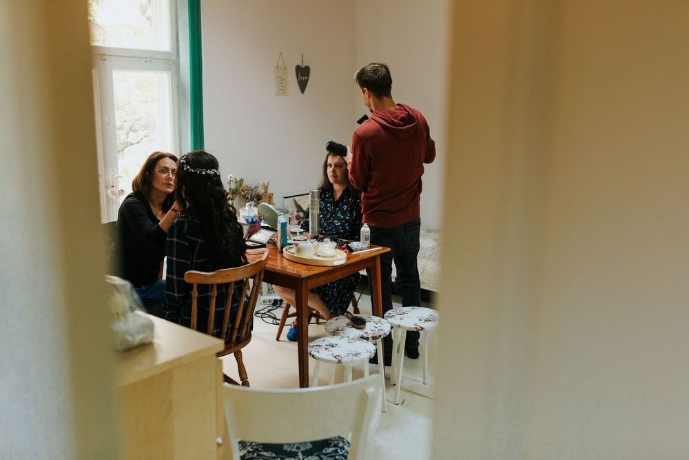 Small group of wedding guests conversing around a table in a bright room with large windows.