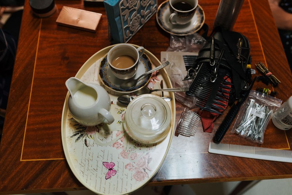 Overhead view of wooden vanity table with tea set, hair tools, and beauty accessories during bridal prep.