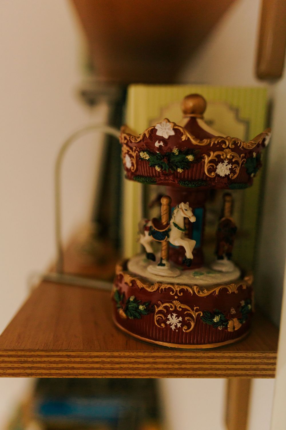 Decorative vintage carousel music box figurine displayed on wooden shelf with ornate gold detailing.