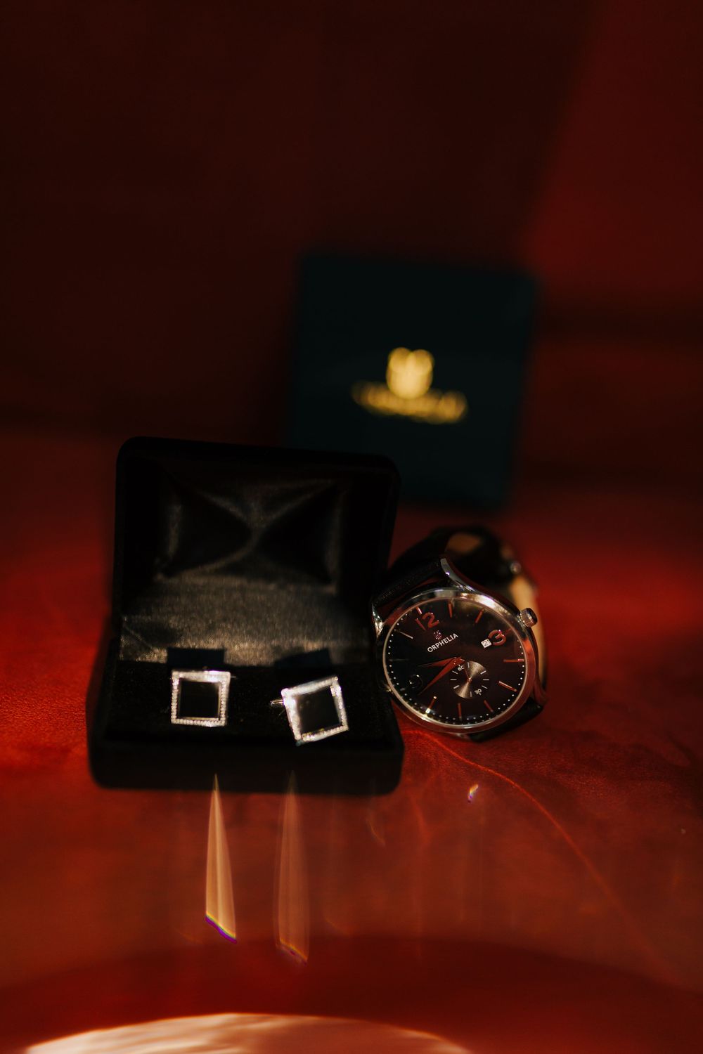 Elegant groom accessories including silver cufflinks in black velvet box and luxury wristwatch on red surface.
