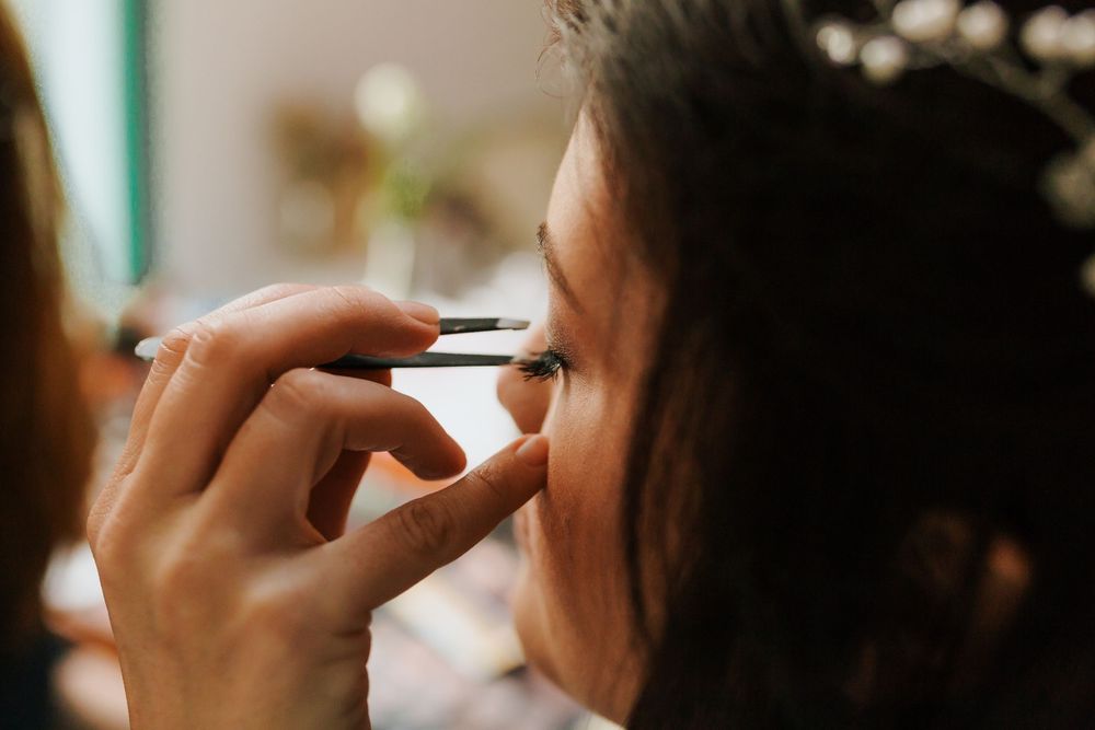 Close-up of makeup artist applying eyeliner to bride with dark curly hair before wedding ceremony.