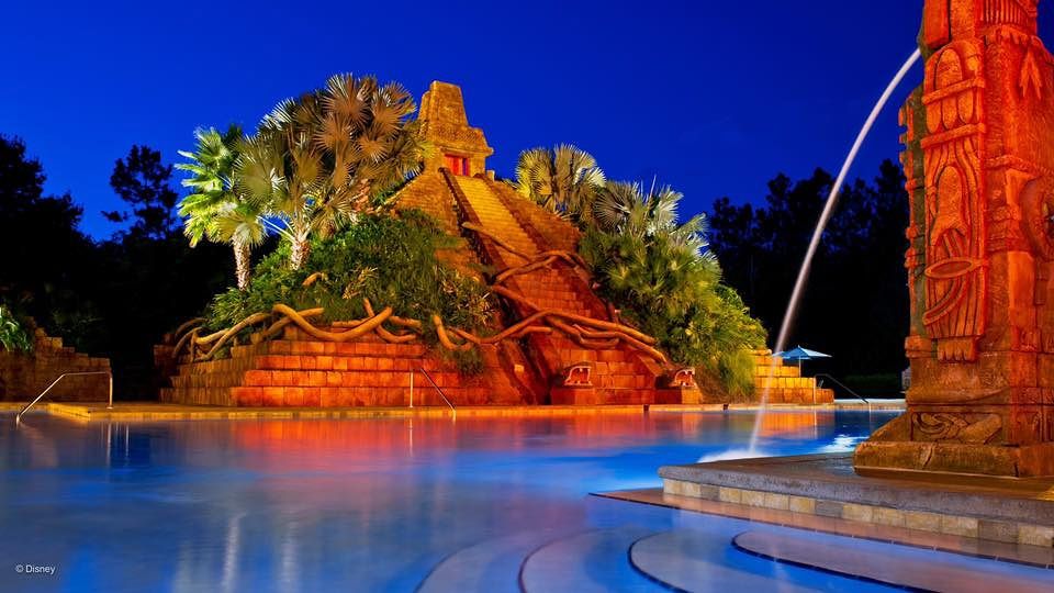 Illuminated pool area with dramatic red rock formations and tropical landscaping at night.
