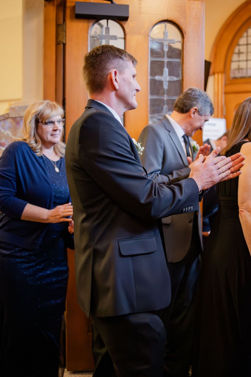 Wedding guests in formal attire clap and celebrate inside a church during a wedding ceremony reception.