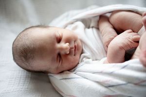 Peaceful newborn baby swaddled in white blanket sleeping soundly with tiny hands visible.